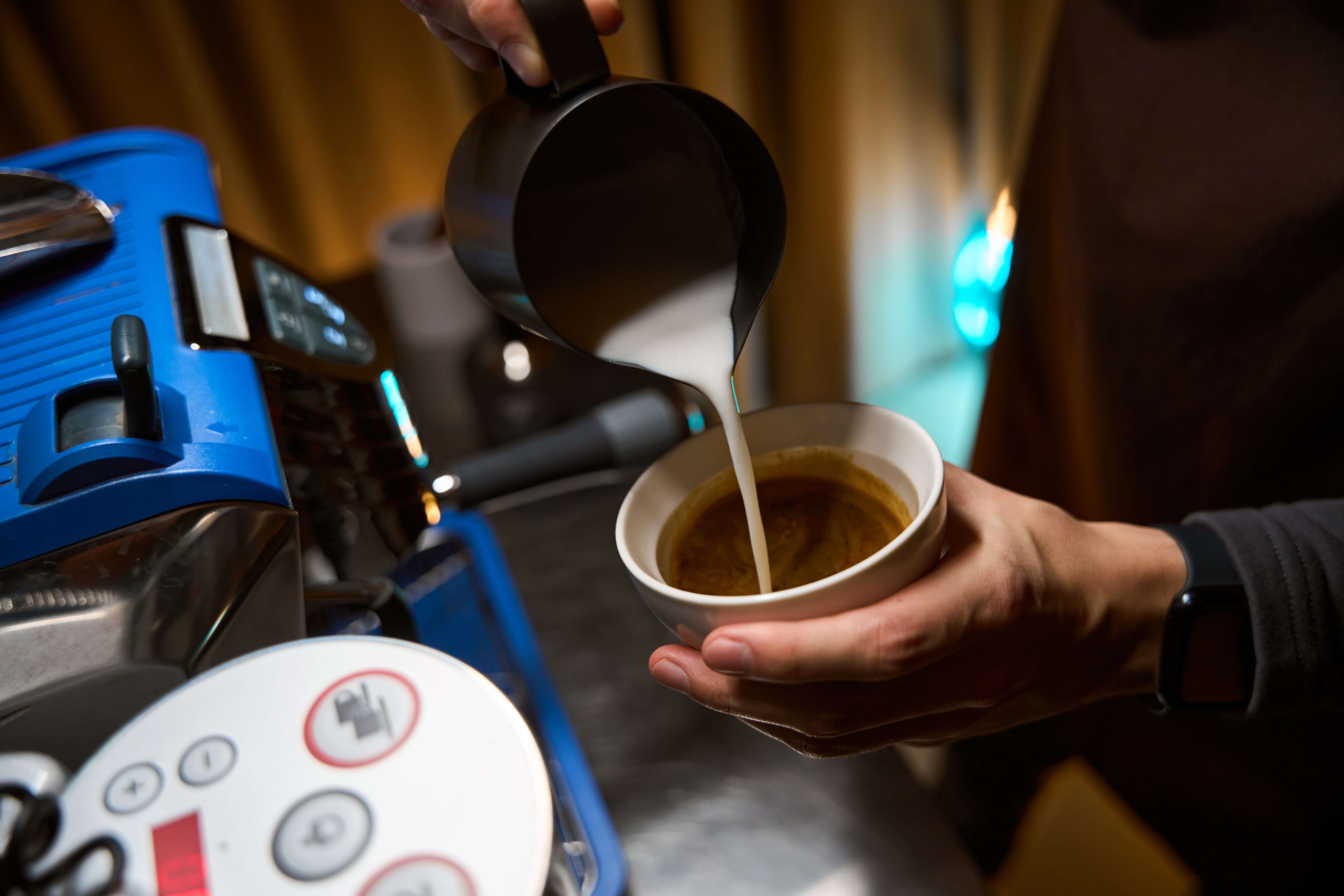 Barista adding milk in cup with coffee while preparing tasty cappuccino